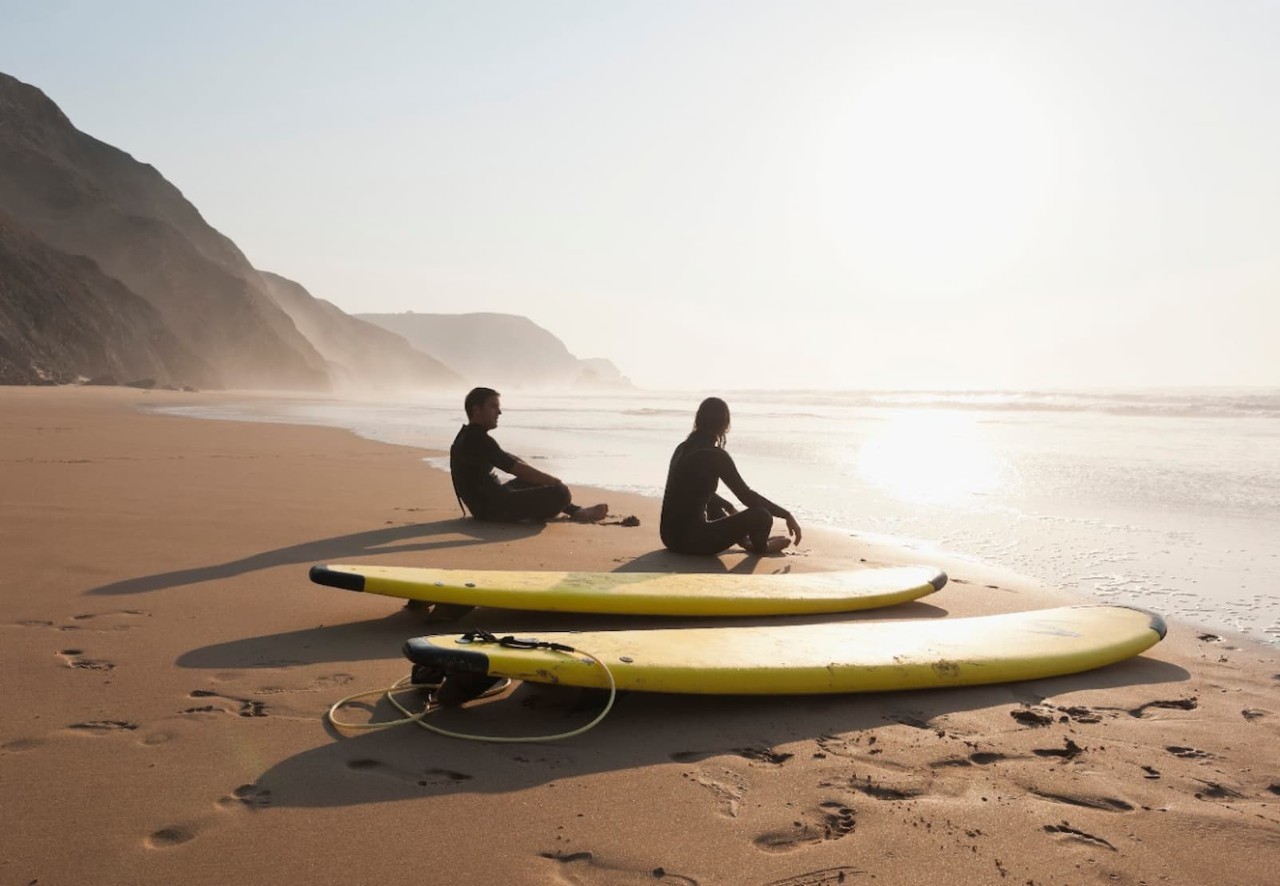 two surfers sitting on sand beside surfboards